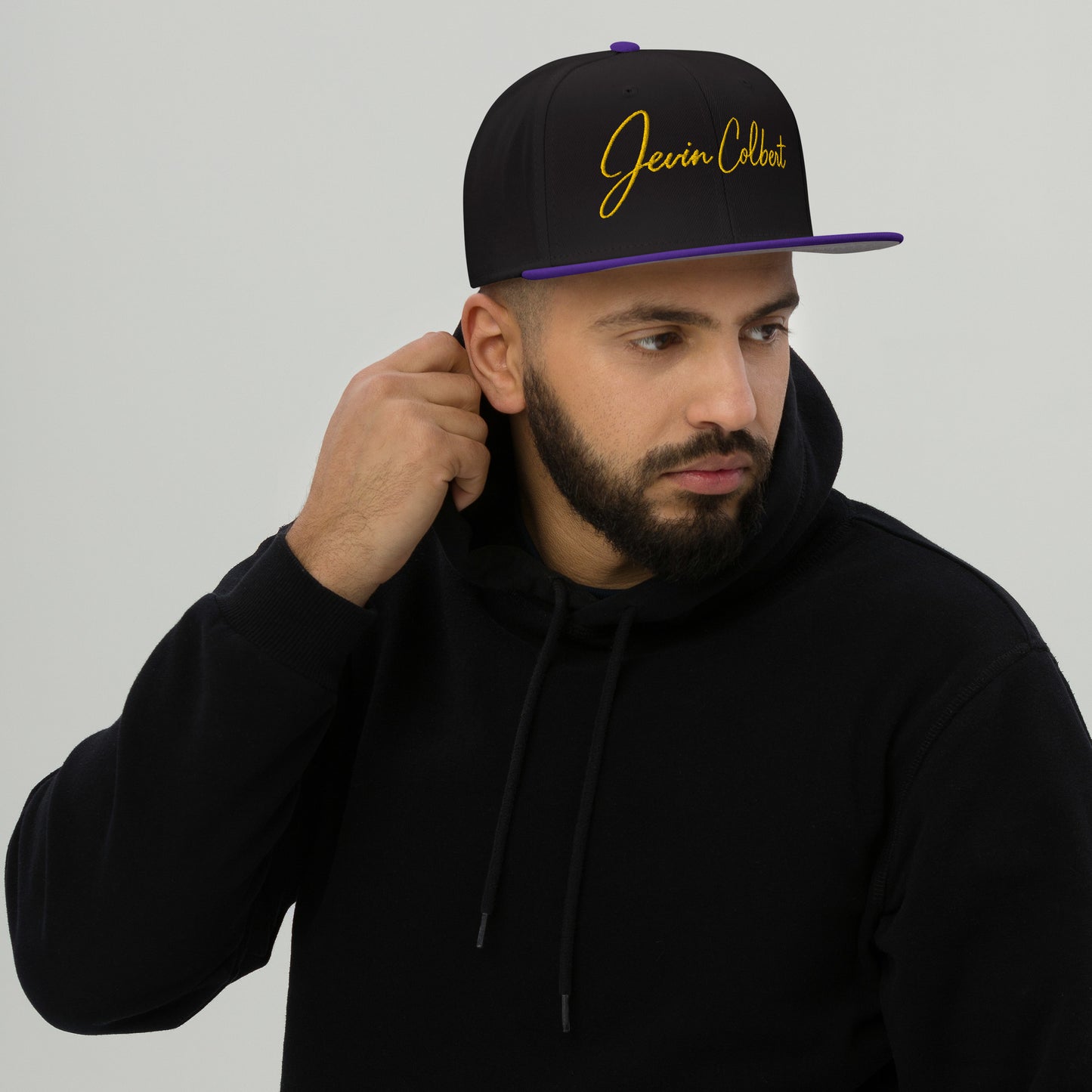 Black snapback cap with Jevin Colbert logo and purple flat brim