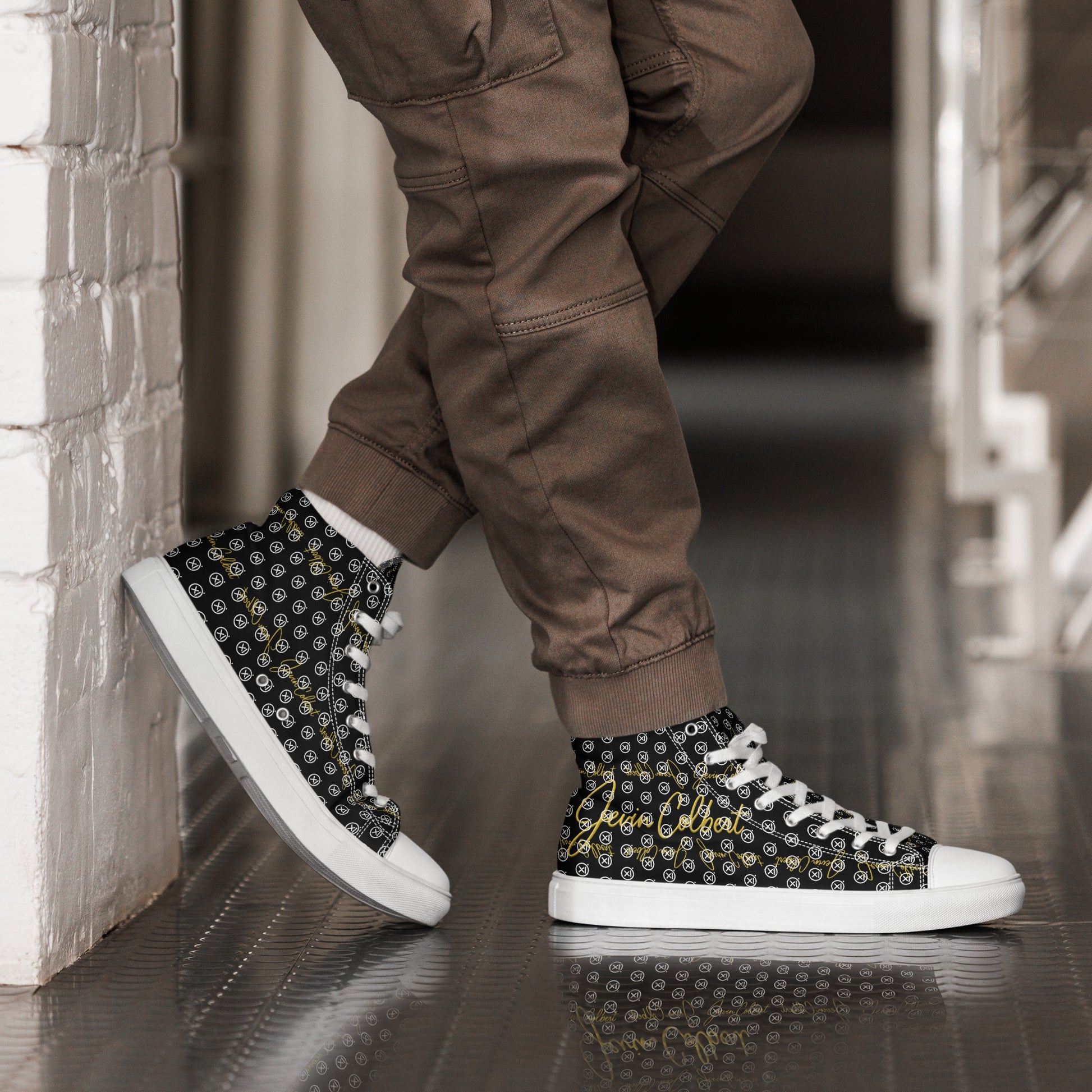 Black high-top canvas sneakers with gold-and-white monogram print and white laces on feet