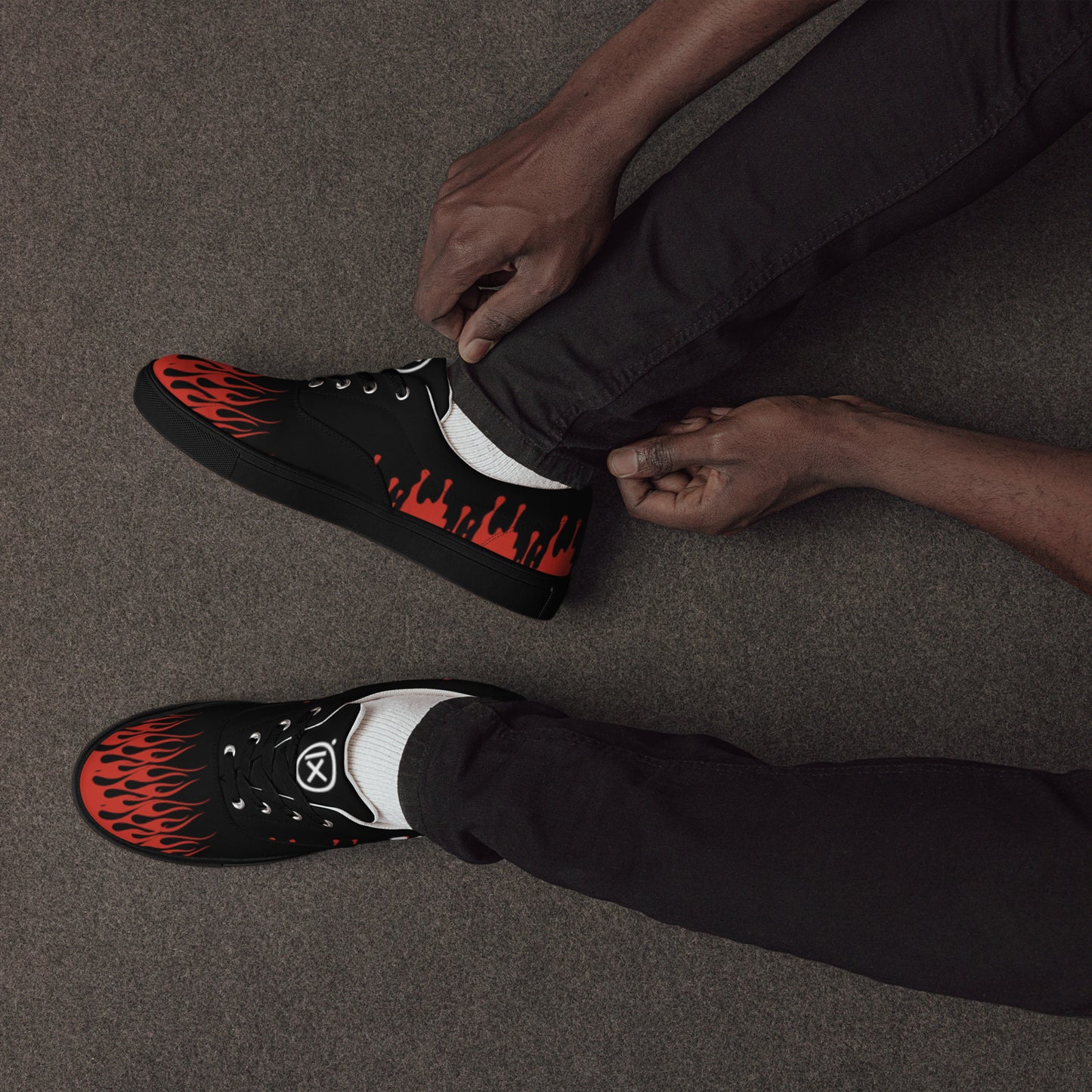 Black canvas sneakers with red flame graphic, worn with dark pants, sitting side view.