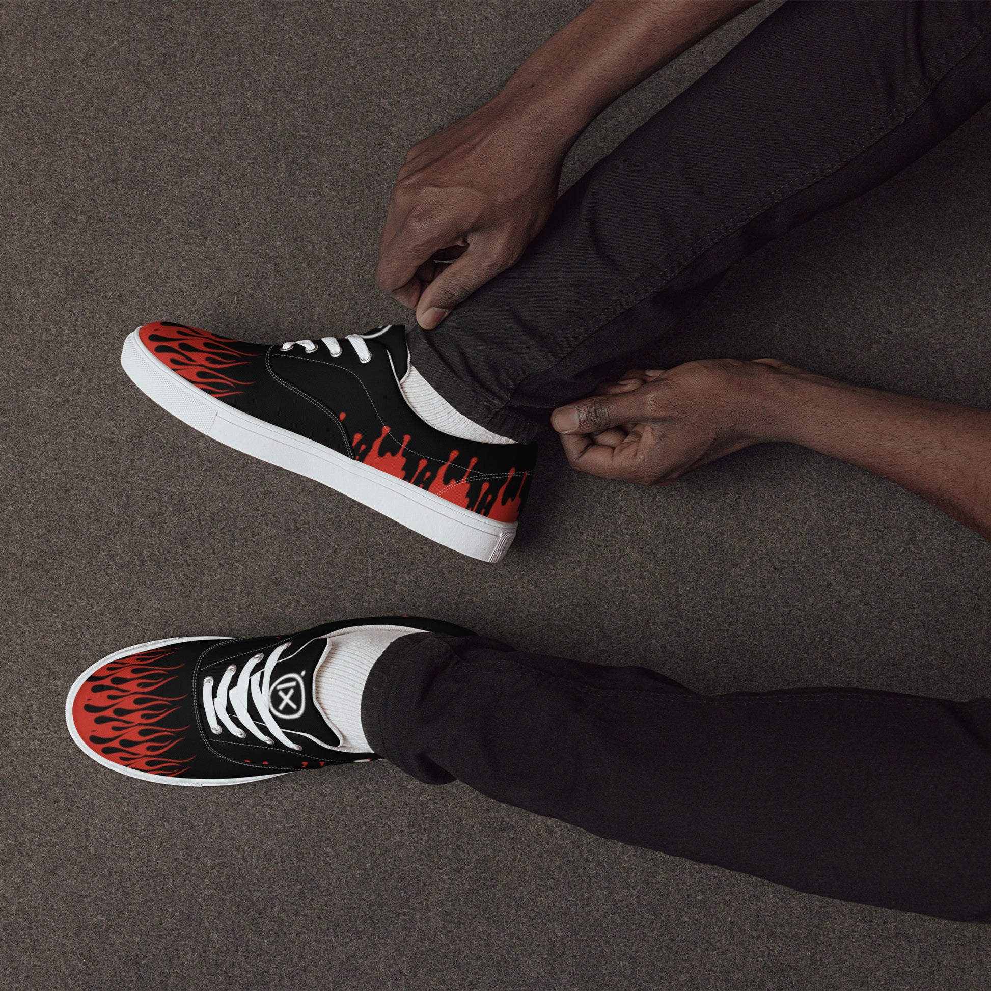 Black canvas sneakers with red flame graphic, worn with dark pants, sitting side view.