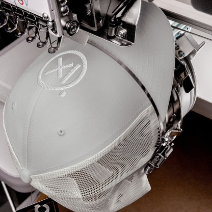 Retro trucker snapback cap in light gray with mesh side panels and circular logo patch