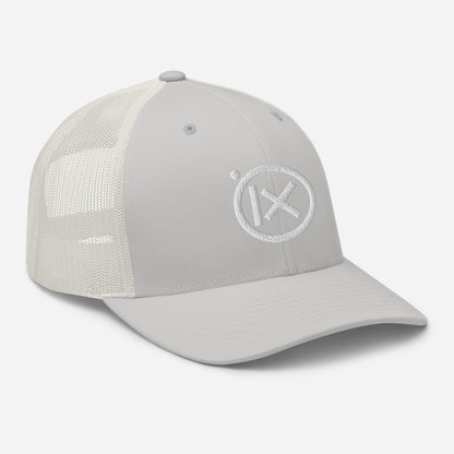 White trucker snapback cap with circular X logo patch on front panel and white mesh back.