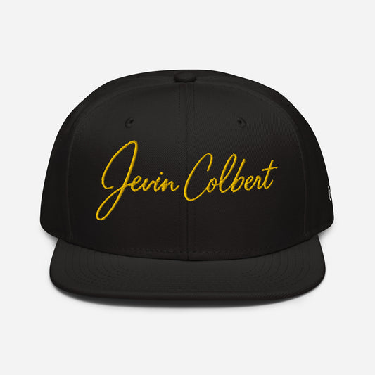 Black snapback cap with yellow “Jevin Colbert” script embroidery on the front panel