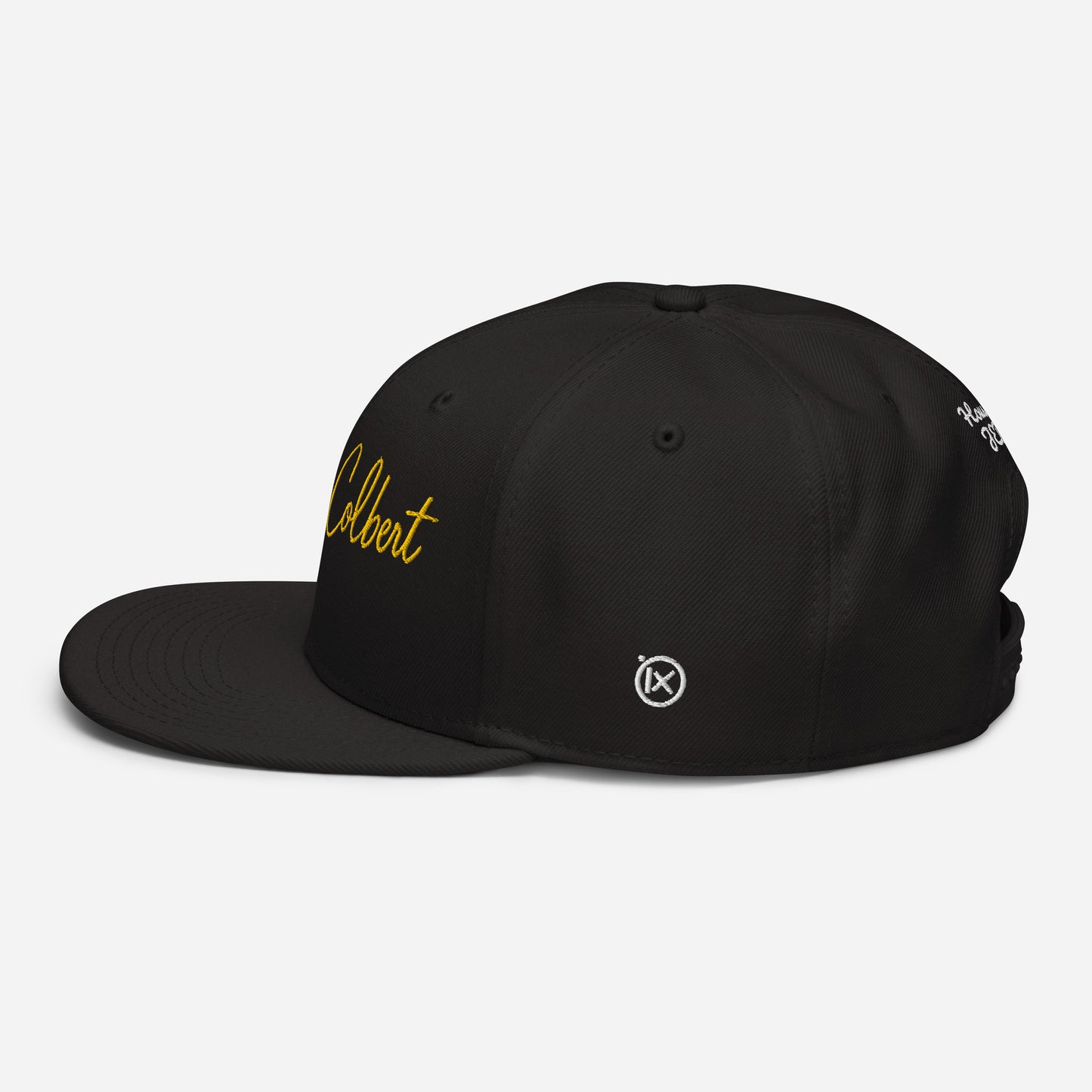 Black snapback cap with yellow “Colbert” script logo and small emblem on the side