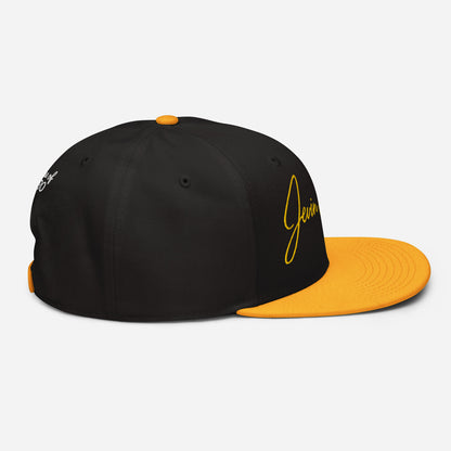 Black snapback cap with orange underside brim and yellow logo patch on side